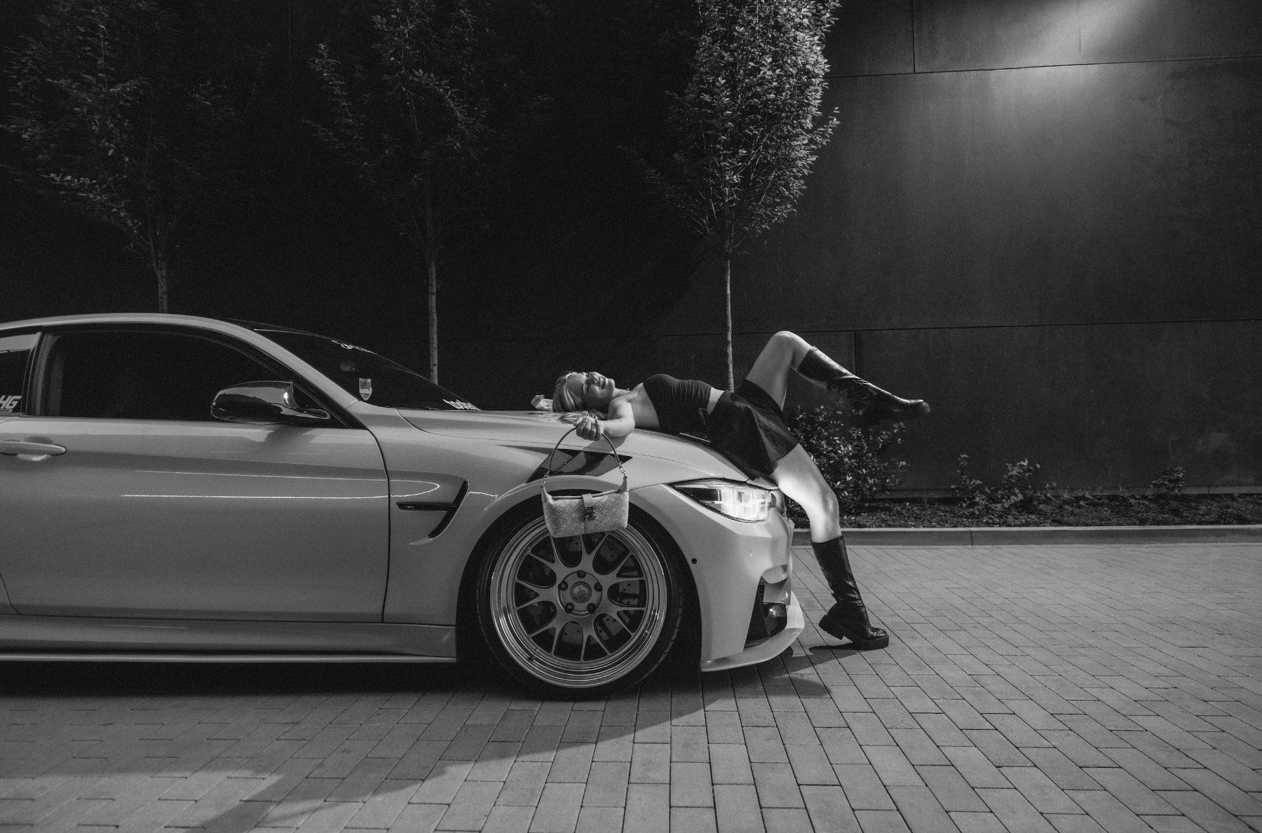 Model liegt auf der Haube eines BMW M4, Schwarzweiß – Fusion-Shooting für Jini Cars