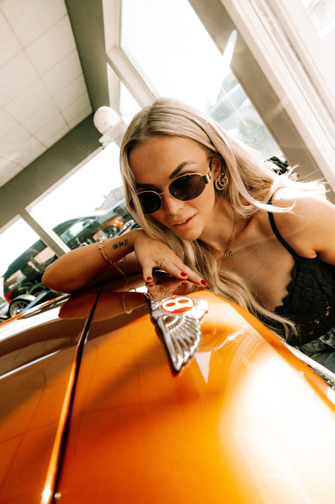 Frau am orangefarbenen Bentley, Portrait über dem Emblem – Automotive-Porträtfotografie